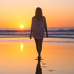 Image showing Lady walking on sandy beach in sunset.