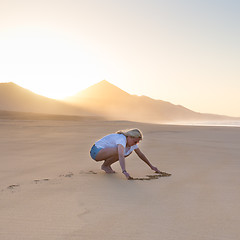 Image showing Lady drawing heart shape in sand on beach.