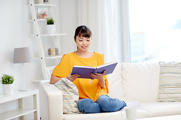 Image showing smiling young asian woman reading book at home