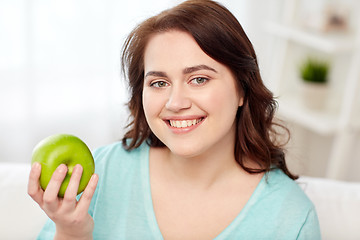 Image showing happy plus size woman eating green apple at home