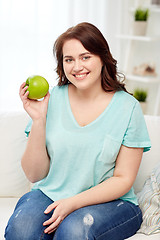 Image showing happy plus size woman eating green apple at home