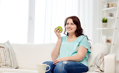 Image showing happy plus size woman eating green apple at home