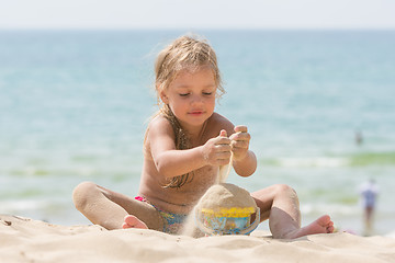 Image showing Little five-year girl pours sand into bucket baby on the sea beach