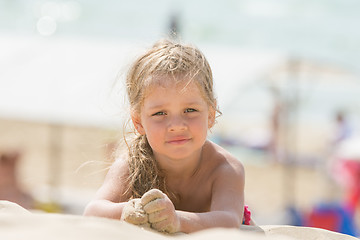 Image showing Dissatisfied girl four years lies on the beach sand on his stomach and looks in the frame