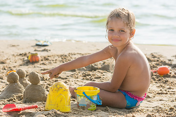 Image showing Pleased with the child on a sandy beach at the water points at cakes hired by sand