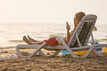 Image showing Pregnant woman lying on a sun lounger on the beach and looking at the phone