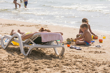 Image showing On the sea beach near the water with sunbathing chaise longue Woman and children playing in the sand