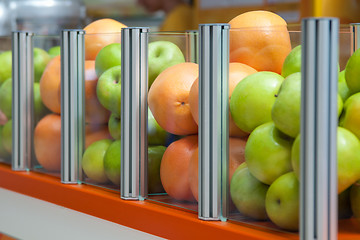 Image showing A large glass container showcase fresh fruit apples and oranges, focus is positioned on oranges
