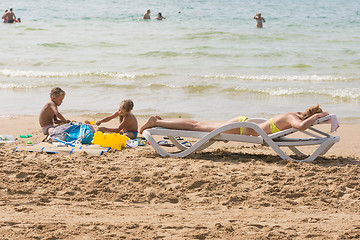 Image showing On the beach near the water with a beach chair sunbathing woman near the children playing in the sand