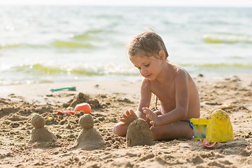 Image showing The child sits on the sandy beach of the reservoir and enthusiasm molds of sand cakes