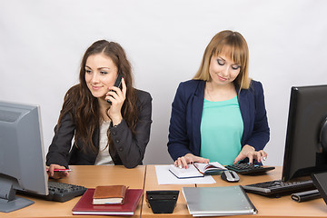 Image showing  Office colleagues girl sitting behind a desk, with a phone, the other with a calculator