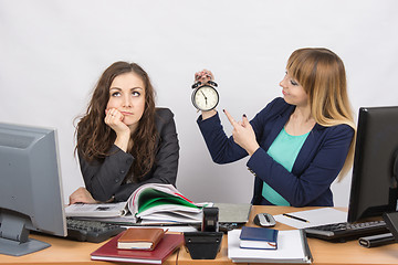 Image showing Office employee working at the end of the day, one with a smile, indicating the clock, the other thoughtfully props head