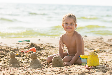 Image showing The child sits on the waterfront and sculpts sand cakes