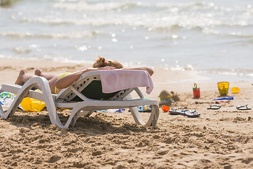 Image showing On the sea beach near the water with a beach chair sunbathing girl, spanking and childrens sand toys