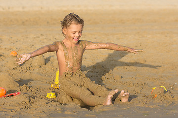 Image showing Satisfied six year old girl to roll yourself wet sand on the beach