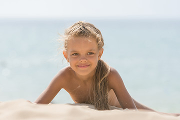 Image showing Six-year Tanned girl lying on sand, leaning on hands against the sea