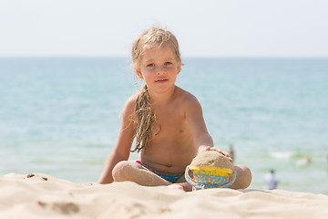 Image showing Baby girl playing with sand and vederochkom child on the sea beach