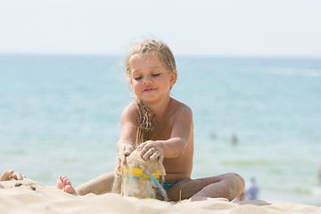 Image showing Pretty girls four years playing in the sand with a child on the sea beach bucket