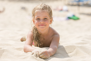 Image showing Pretty girls four years lying in the sand on his stomach on the beach on a sunny day