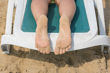 Image showing On a sun lounger are female legs soiled in sand heels top