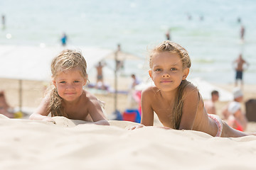 Image showing Two girls lying on the sand on the beach and look at the frame