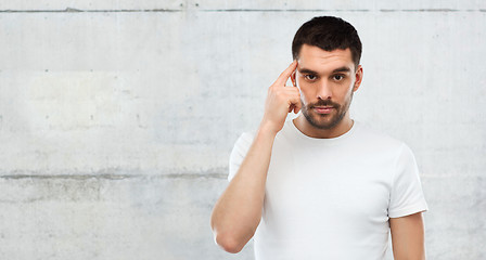 Image showing man with finger at temple over gray wall