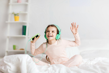 Image showing girl sitting on bed with smartphone and headphones