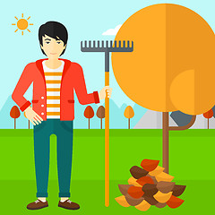 Image showing Man with rake standing near tree and heap of autumn leaves.