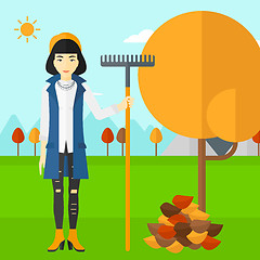 Image showing Woman with rake standing near tree and heap of autumn leaves.