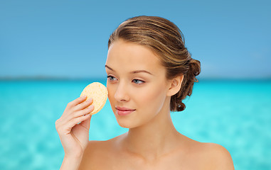 Image showing young woman cleaning face with exfoliating sponge