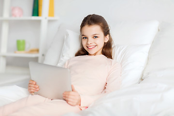 Image showing happy girl lying in bed with tablet pc at home