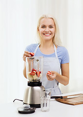 Image showing smiling woman with blender preparing shake at home