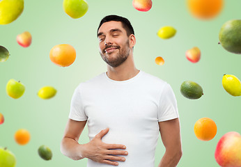 Image showing happy full man touching tummy over falling fruits