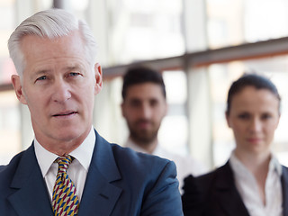 Image showing portrait of senior businessman as leader  with staff in backgrou