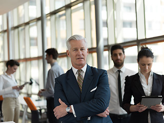 Image showing portrait of senior businessman as leader  with staff in backgrou