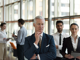 Image showing portrait of senior businessman as leader  with staff in backgrou