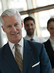 Image showing portrait of senior businessman as leader  with staff in backgrou