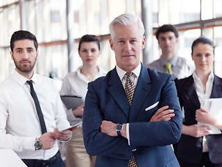 Image showing portrait of senior businessman as leader  with staff in backgrou