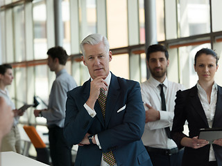 Image showing portrait of senior businessman as leader  with staff in backgrou