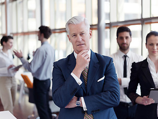 Image showing portrait of senior businessman as leader  with staff in backgrou