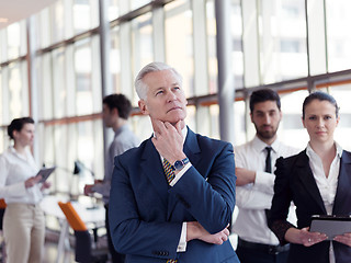 Image showing portrait of senior businessman as leader  with staff in backgrou