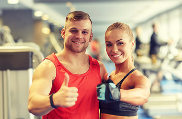 Image showing smiling man and woman showing thumbs up in gym