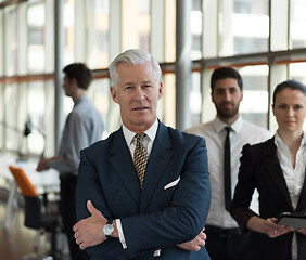 Image showing portrait of senior businessman as leader  with staff in backgrou