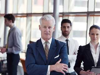 Image showing portrait of senior businessman as leader  with staff in backgrou