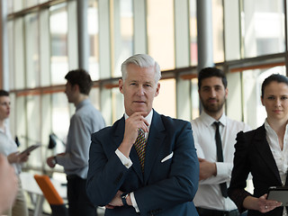 Image showing portrait of senior businessman as leader  with staff in backgrou