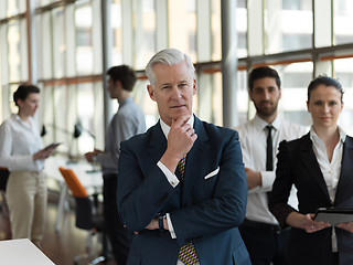 Image showing portrait of senior businessman as leader  with staff in backgrou