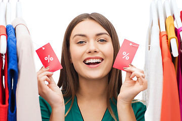 Image showing happy woman with sale tags on clothes at wardrobe