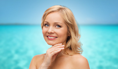 Image showing smiling middle aged woman touching face over sea