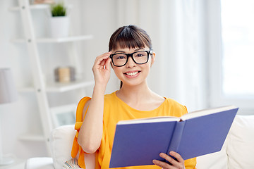 Image showing smiling young asian woman reading book at home