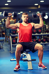 Image showing young man with dumbbells flexing muscles in gym